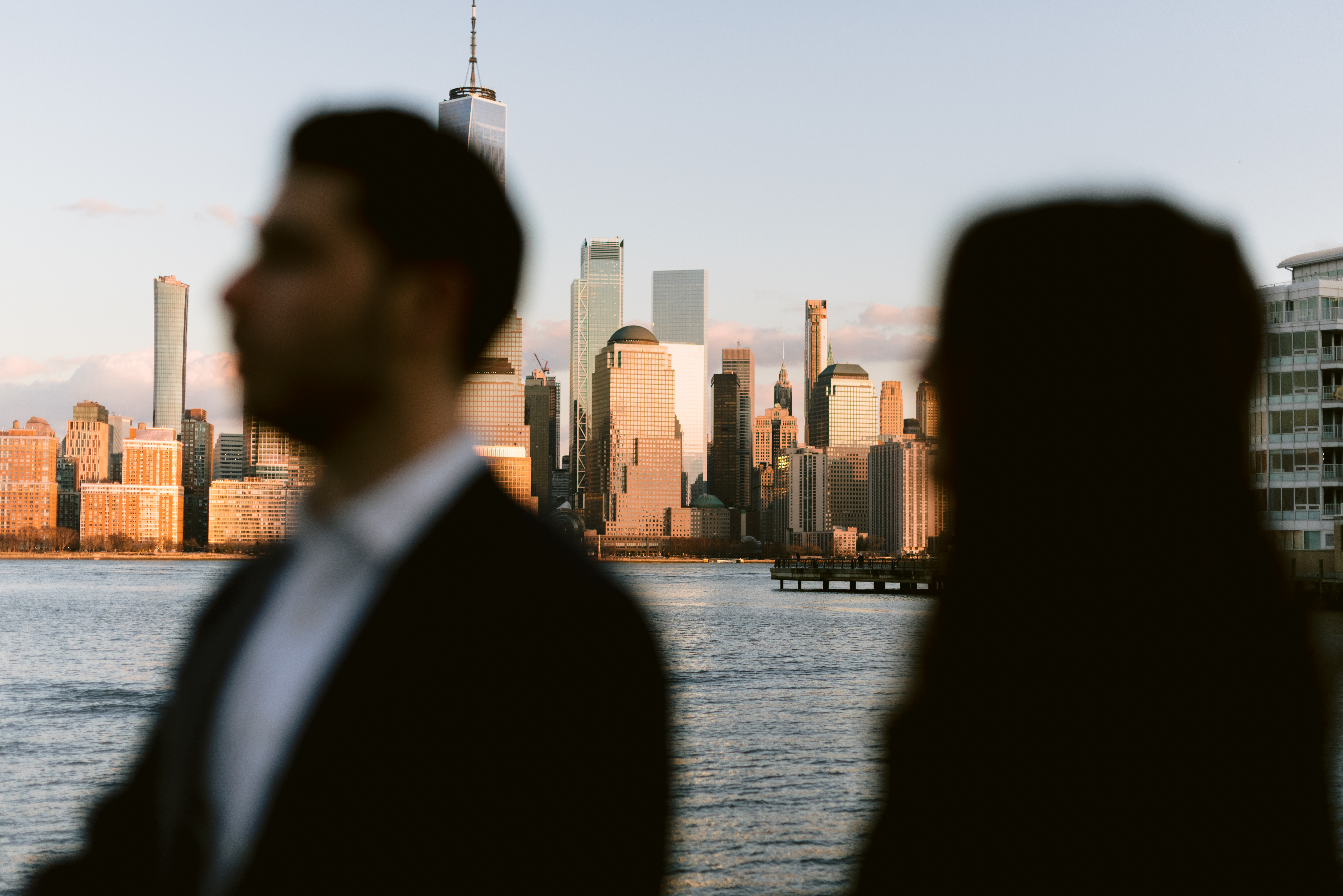 Engaged couple in jersey city in front of sunset on the hudson river with the nyc skyline in the distance