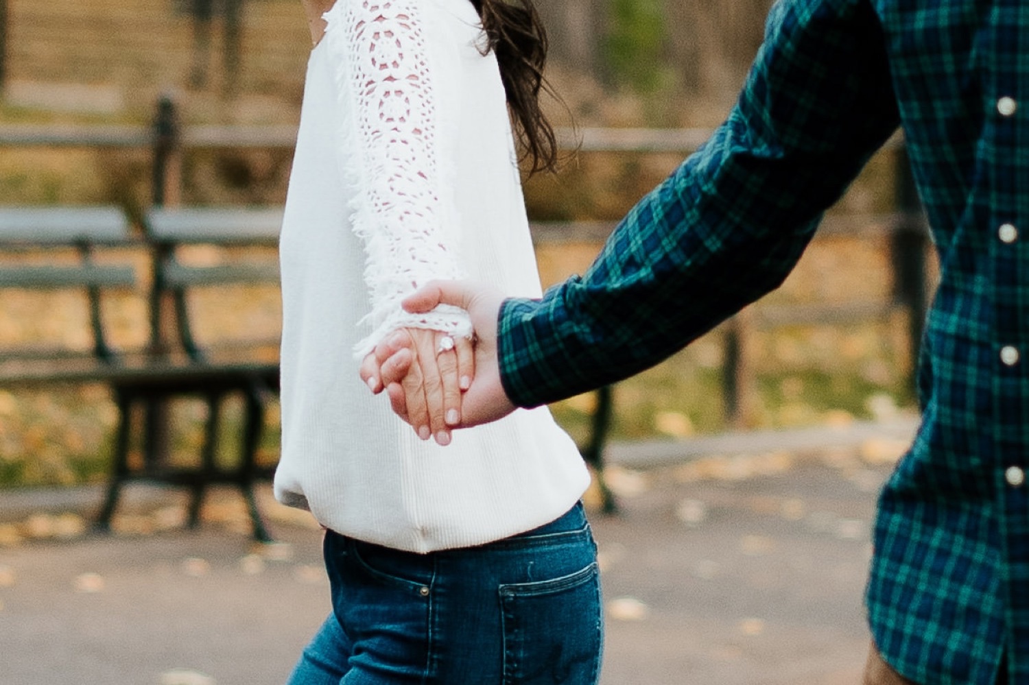 engaged couple holds hands in sight of her engagement ring in central park nyc during engagement photoshoot