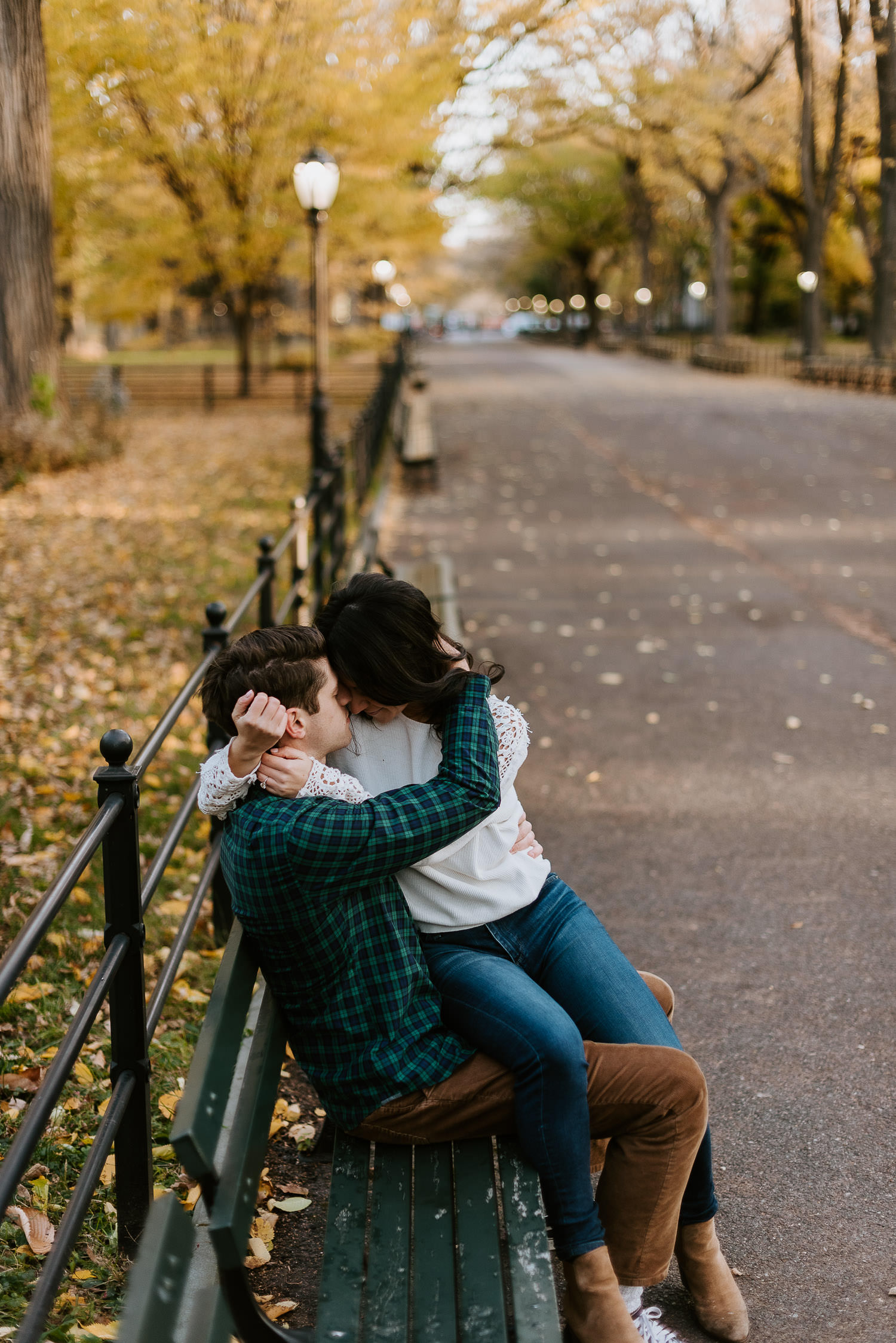 engaged couple sits on bench at literary walk on the mall in central park for their engagement photos